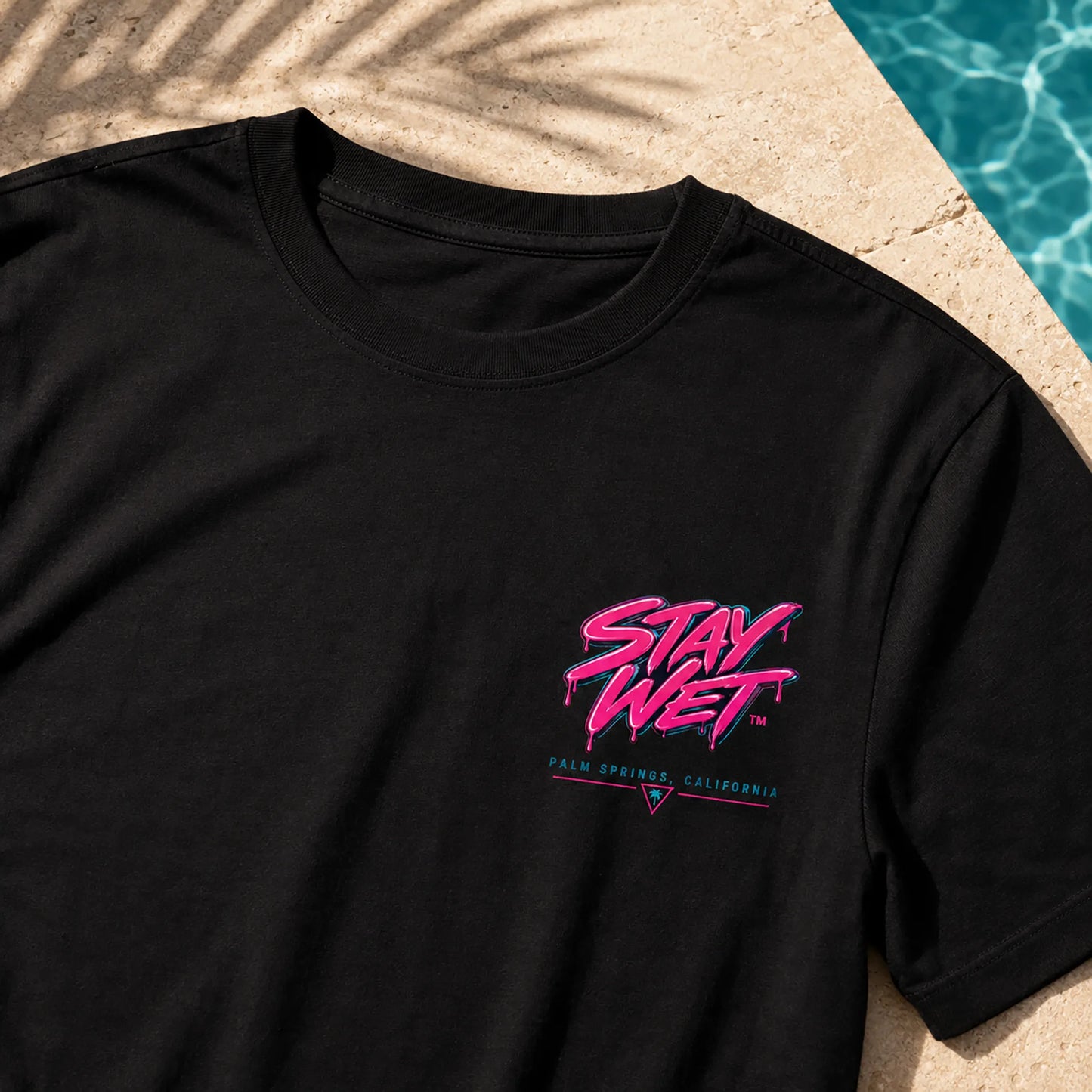 Close-up of the black Stay Wet Palms tee showing the small pink left-chest print