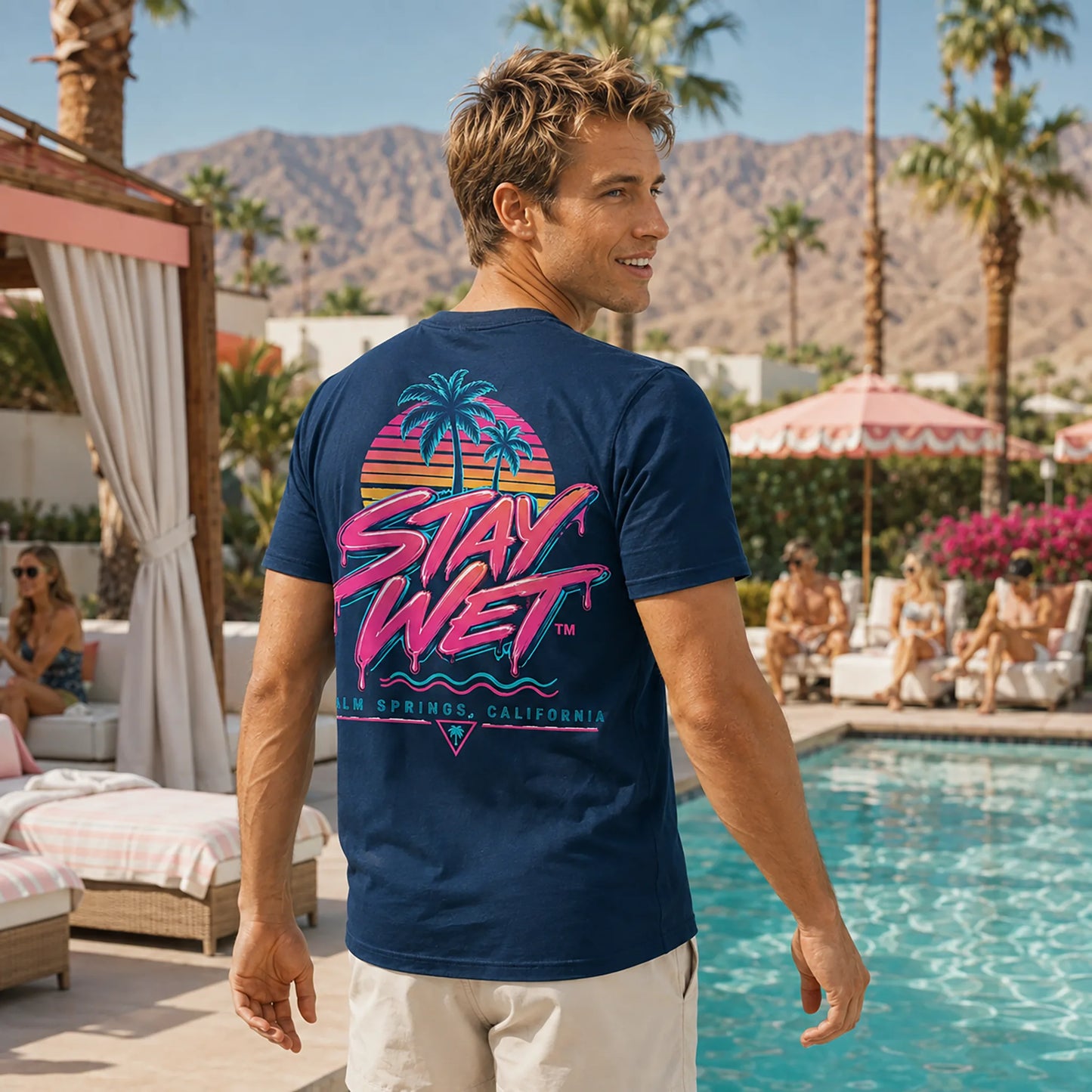 Jackson wearing the navy Stay Wet Palms tee featuring the large neon back graphic at a Palm Springs resort pool
