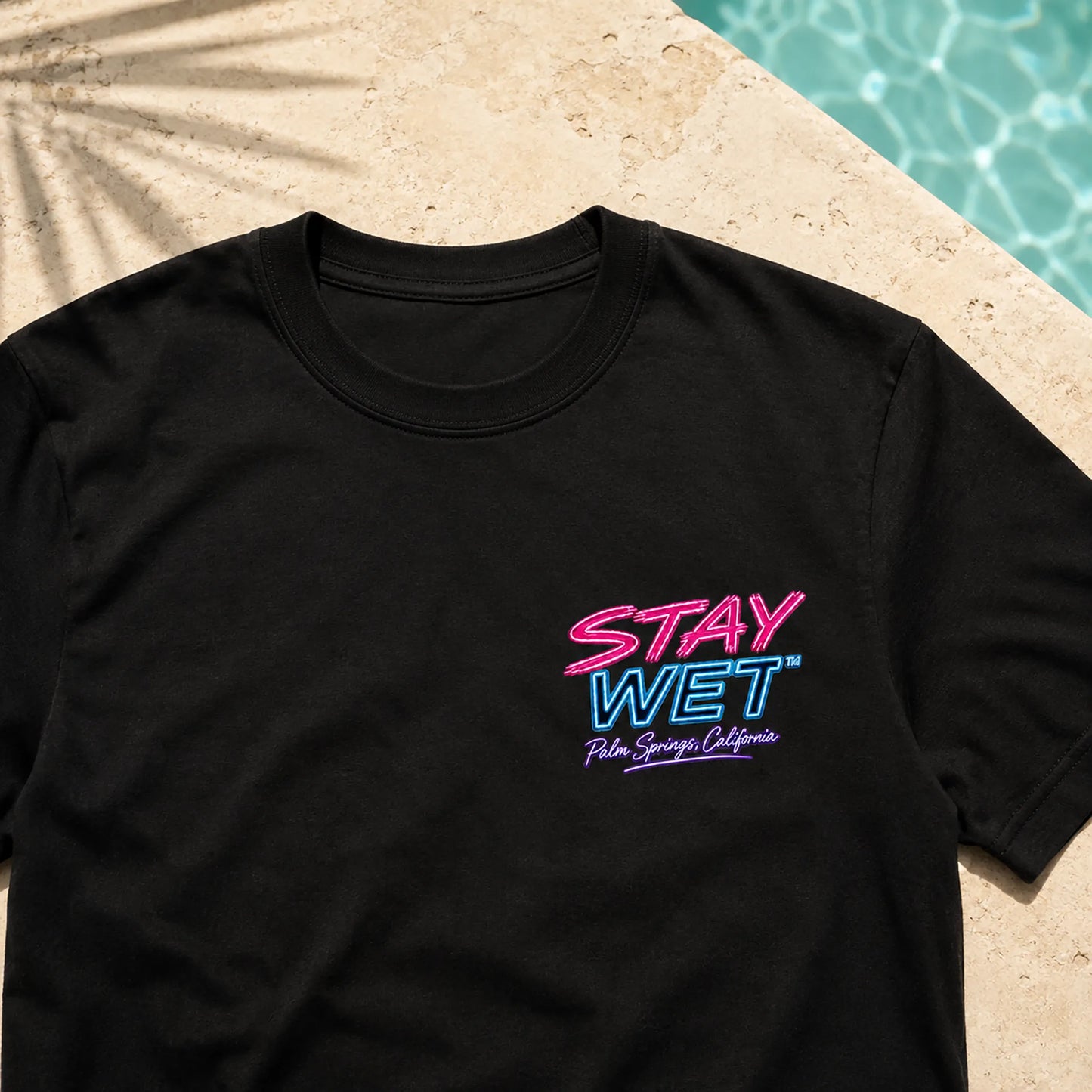 Close-up of the black Stay Wet Poolside Takeover Pink Flamingo tee showing the small neon left-chest print