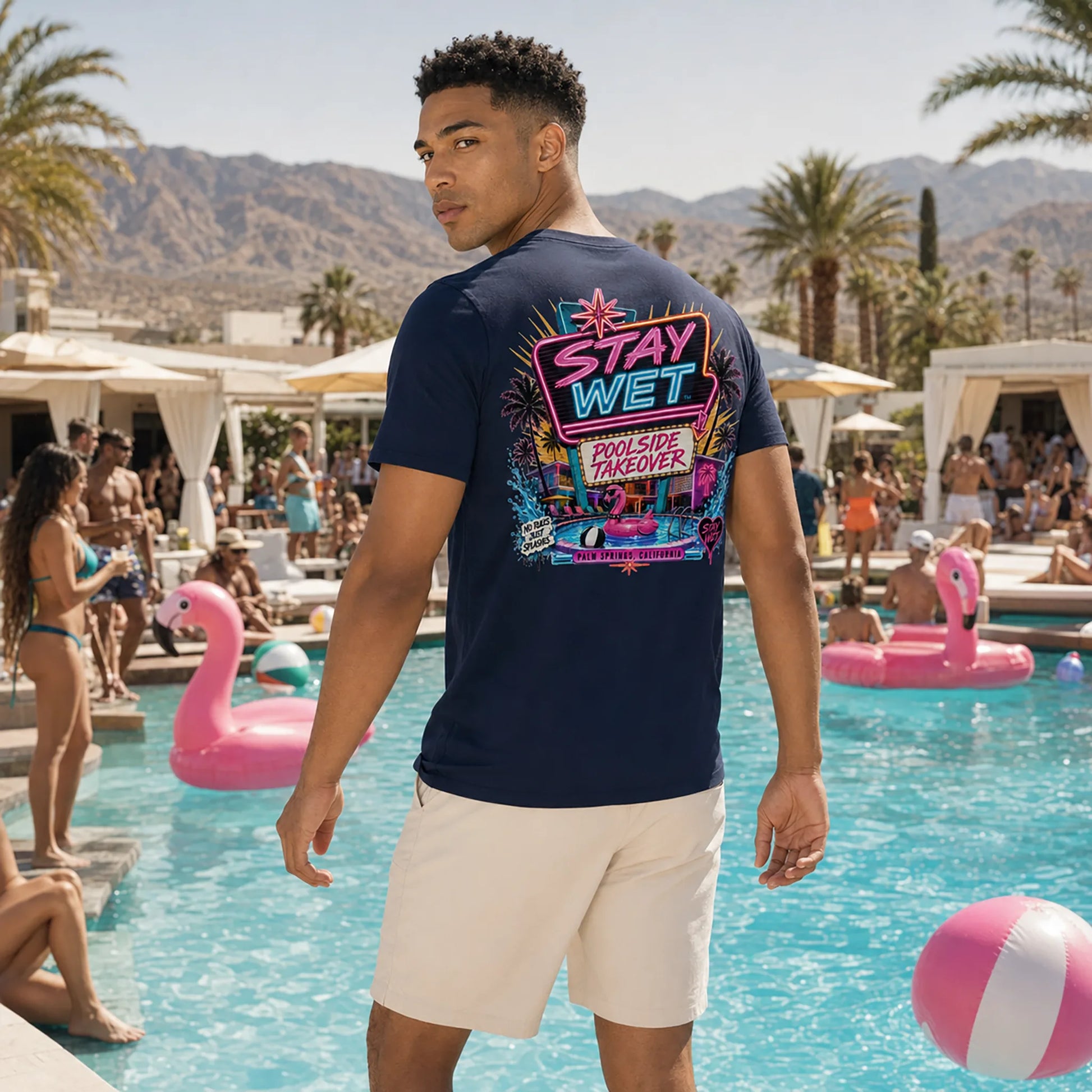 Malik wearing the navy Stay Wet Poolside Takeover Pink Flamingo back-print tee at a Palm Springs pool party